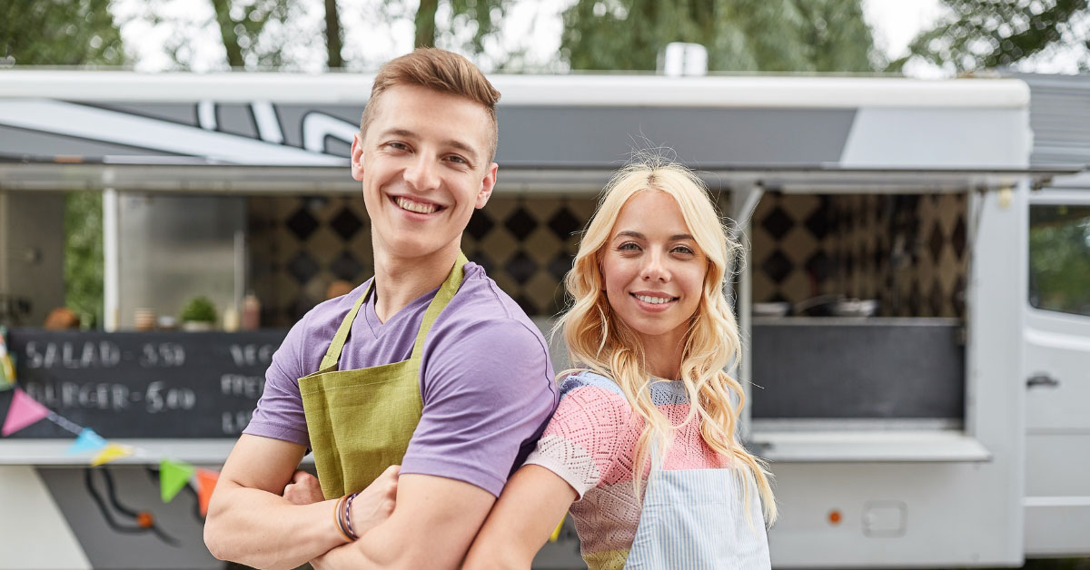 Smiling young adults in aprons in front of a food truck.